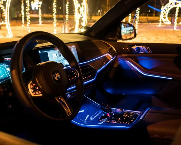 Wnętrze luksusowego BMW x5 nocą, oświetlone niebieskim ambientowym światłem. Za oknem świąteczne iluminacje.
