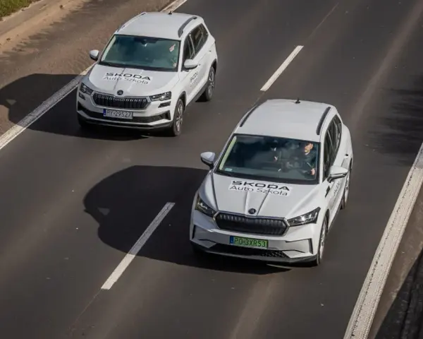 Dwa białe samochody Skoda Auto Szkoła jadą po drodze, gdzie obowiązuje ruch lewostronny.
