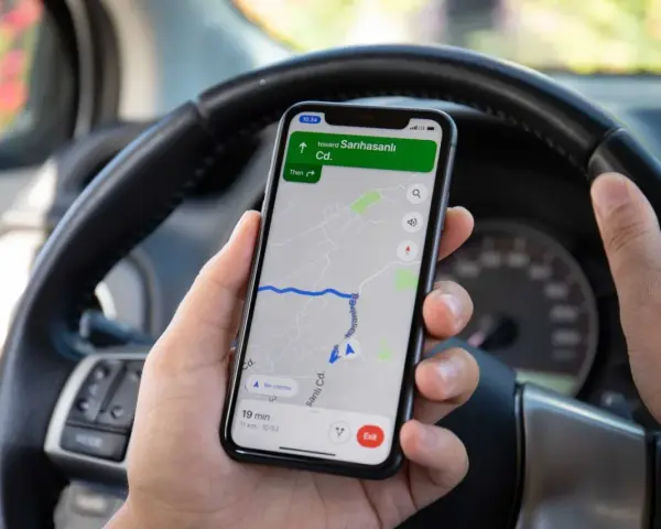 Ręce kierowcy trzymają telefon z nawigacją. Używanie telefonu podczas jazdy grozi mandatem.