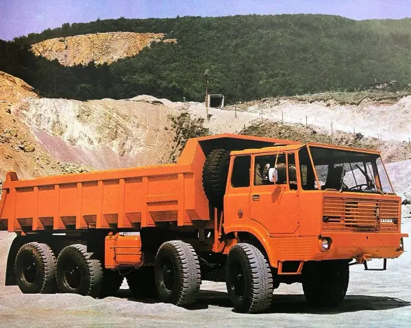 Pomarańczowy wywrotka Tatra 813 z zapasowym kołem na pace, gotowa do pracy w kamieniołomie.