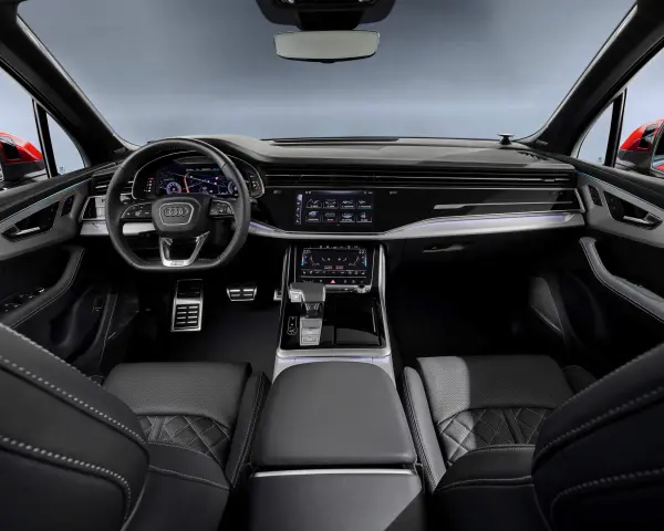 Wnętrze Audi Q7 z ekranami, kierownicą i skórzanymi fotelami.
