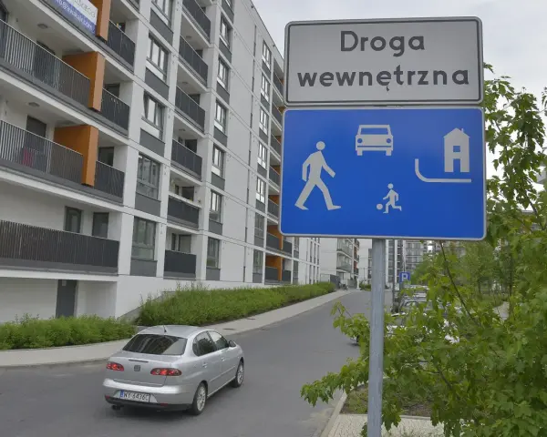 Droga wewnętrzna w terenie zabudowanym. Znak informuje o ruchu pieszych, samochodów i domów.