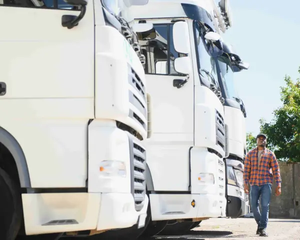 Kierowca idzie obok rzędu białych ciężarówek. To właśnie spedycja co to – transport towarów na dużą skalę.