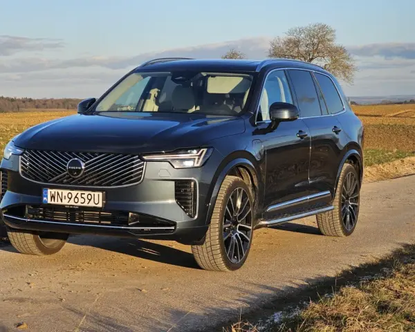 Ciemnoszary Volvo XC90 na polnej drodze, z widokiem na pola i drzewa w tle.