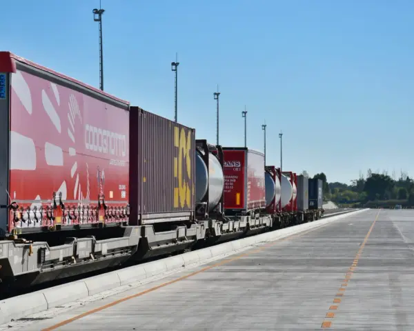 Długi pociąg towarowy z kontenerami, w tym czerwonymi z logo COSCO i żółtymi, czeka na dalszy transport kolejowy.