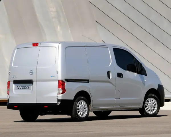 Srebrny Nissan NV200, wszechstronny van, zaparkowany przed nowoczesnym budynkiem.