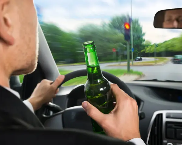 Kierowca z butelką piwa w ręku, jadący na czerwonym świetle. Grozi mu konfiskata samochodu.