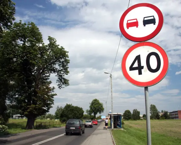 Znaki drogowe: zakaz wyprzedzania i ograniczenie prędkości do 40 km/h. Droga z samochodami i drzewami.