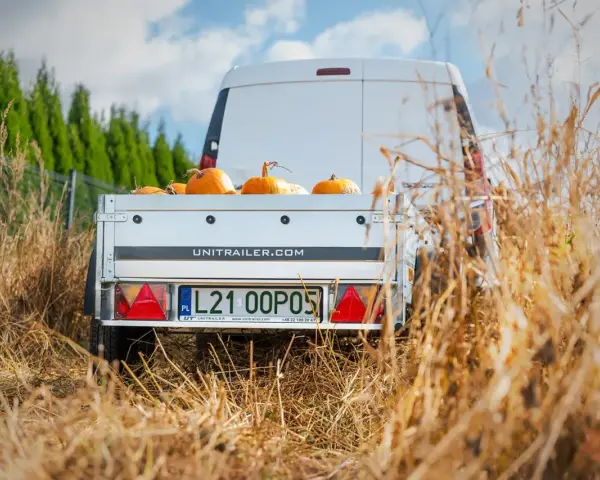 Biała furgonetka z przyczepą pełną dyni, gotowa do transportu. Spedytor czeka na załadunek.