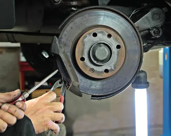 Dłonie mechanika z narzędziami przy hamulcu tarczowym samochodu.