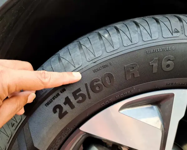 Palec wskazuje na oponę, gdzie widoczny jest rozmiar 215/60 R16. To ważny element, który określa indeks prędkości opon.