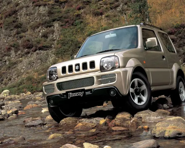 Złoty Suzuki Jimny pokonuje kamienisty strumień. Sprawdź suzuki jimny cena i możliwości terenowe tego kultowego auta.