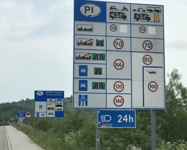 Znaki drogowe przy drodze dwujezdniowej informują o opłatach i limitach prędkości.
