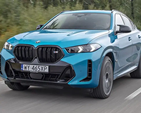 Niebieskie x6 BMW M na drodze, z rozmytym tłem lasu.