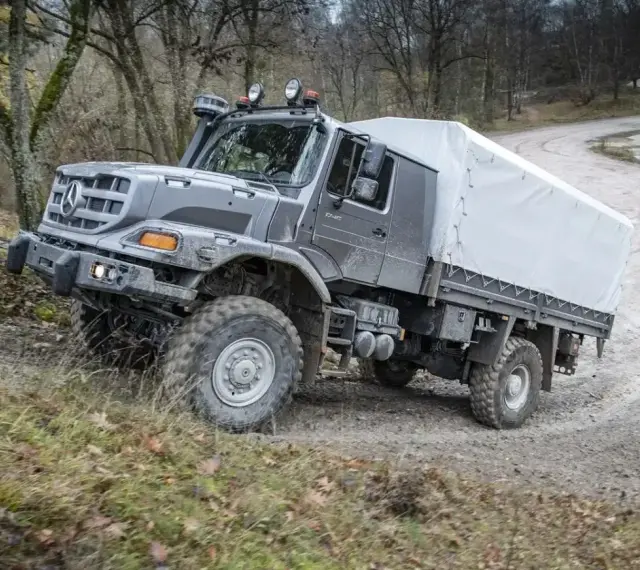 Szary Mercedes Zetros z plandeką pokonuje trudny teren leśnej drogi.