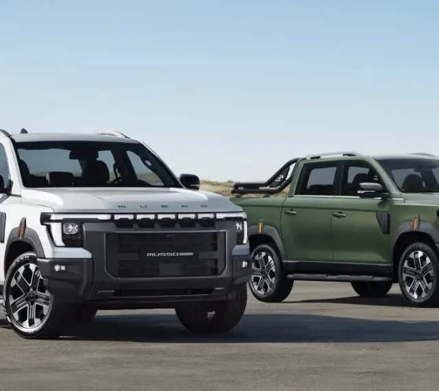 Dwa SsangYong pickup: biały i zielony, stojące na tle plaży i wydm.