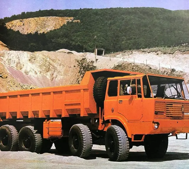 Pomarańczowy wywrotka Tatra 813 z zapasowym kołem na pace, gotowa do pracy w kamieniołomie.