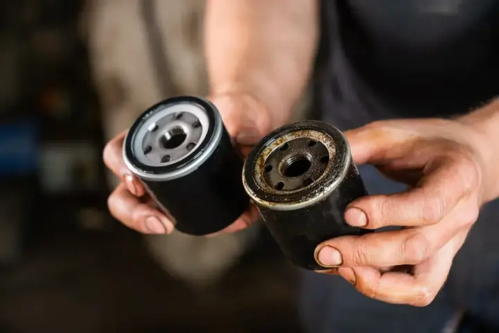 Nowy i zużyty filtr oleju w dłoniach mechanika. Wymiana filtra oleju to kluczowy element dbania o silnik.