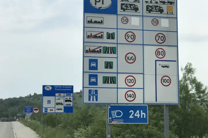 Znaki drogowe przy drodze dwujezdniowej informują o opłatach i limitach prędkości.
