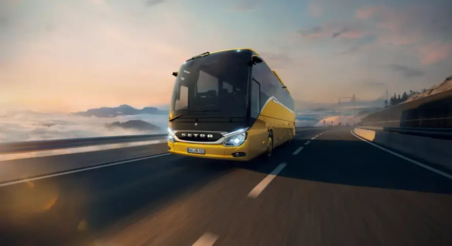 Żółty setra autobus pędzi po autostradzie wśród chmur i gór, w stronę mostu.