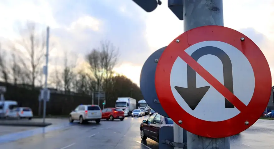 Znak zakazu zawracania na skrzyżowaniu. Samochody stoją w deszczu, czekając na zielone światło.