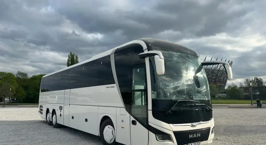 Biały MAN Lion's Coach, nowoczesny autokar turystyczny, zaparkowany na żwirowym placu pod pochmurnym niebem.