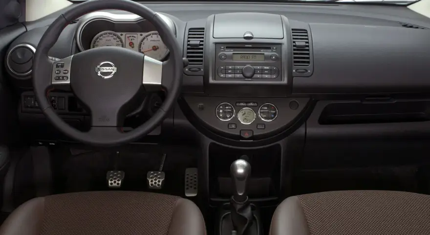 Wnętrze Nissan Note E11: kierownica, deska rozdzielcza z radiem i zegarami, dźwignia zmiany biegów, fotele.