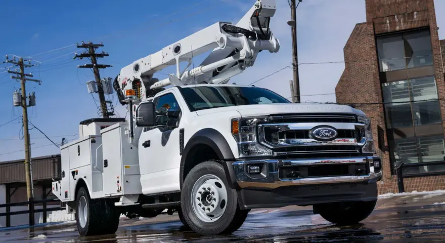 Biały Ford F-750 z podnośnikiem koszowym gotowy do pracy przy liniach energetycznych.