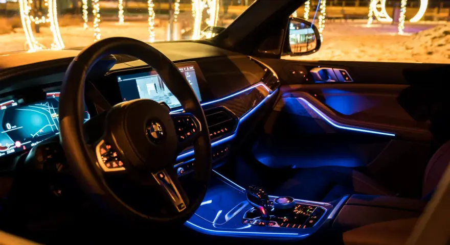 Wnętrze luksusowego BMW x5 nocą, oświetlone niebieskim ambientowym światłem. Za oknem świąteczne iluminacje.