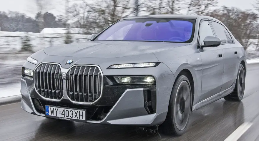 Szary BMW Serii 7 w ruchu, z widocznym grillem i reflektorami. Sprawdź aktualną bmw 7 cena.
