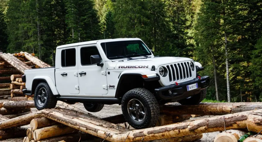 Biały jeep pickup Rubicon pokonuje przeszkodę z bali drewna w lesie.