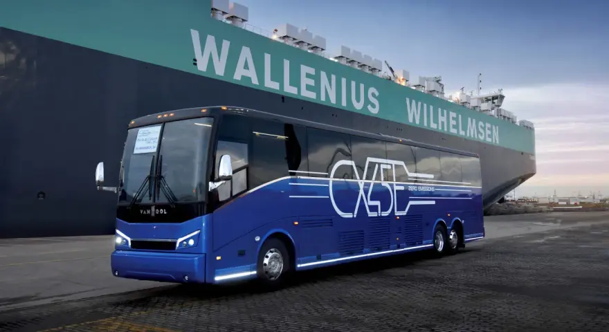 Niebieski autokar Van Hool CX45 z napisem "ZERO EMISSIONS" stoi przy ogromnym statku Wallenius Wilhelmsen.