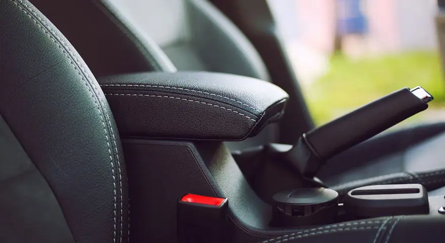 Wnętrze samochodu: czarna skórzana tapicerka, podłokietnik, hamulec ręczny i przycisk auto hold.