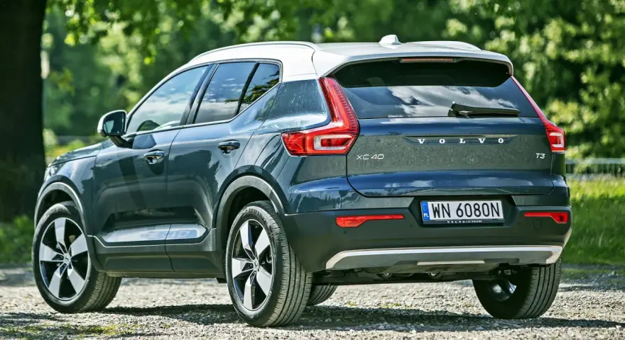 Tylna część ciemnoszarego Volvo XC40 z białym dachem, zaparkowanego na żwirowej drodze. Sprawdź aktualną volvo xc40 cena.