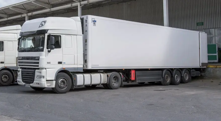 Biała naczepa DAF XF z chłodnią, gotowa do transportu. Obok stoi kolejna ciężarówka, tworząc zgrany zespół pojazdów.