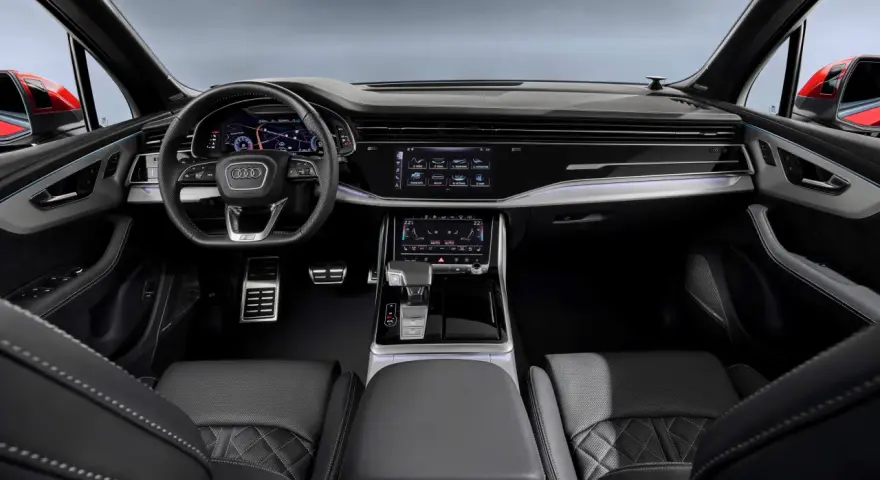 Wnętrze Audi Q7 z ekranami, kierownicą i skórzanymi fotelami.