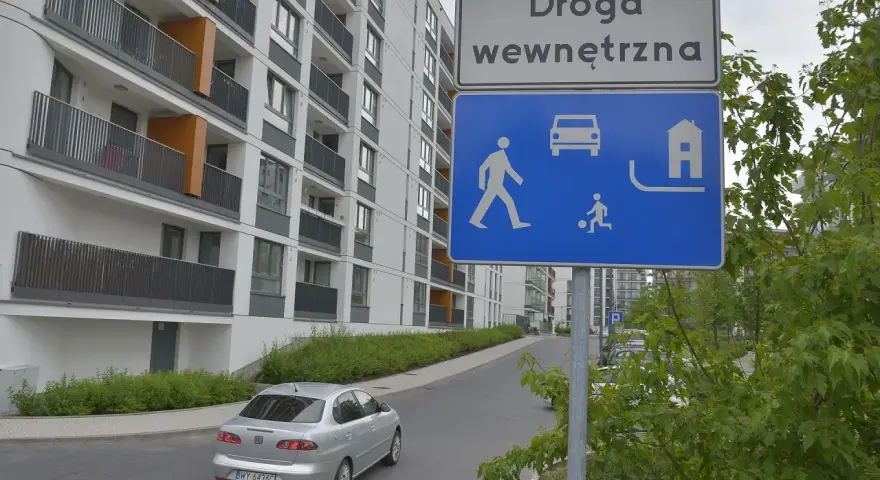 Droga wewnętrzna w terenie zabudowanym. Znak informuje o ruchu pieszych, samochodów i domów.