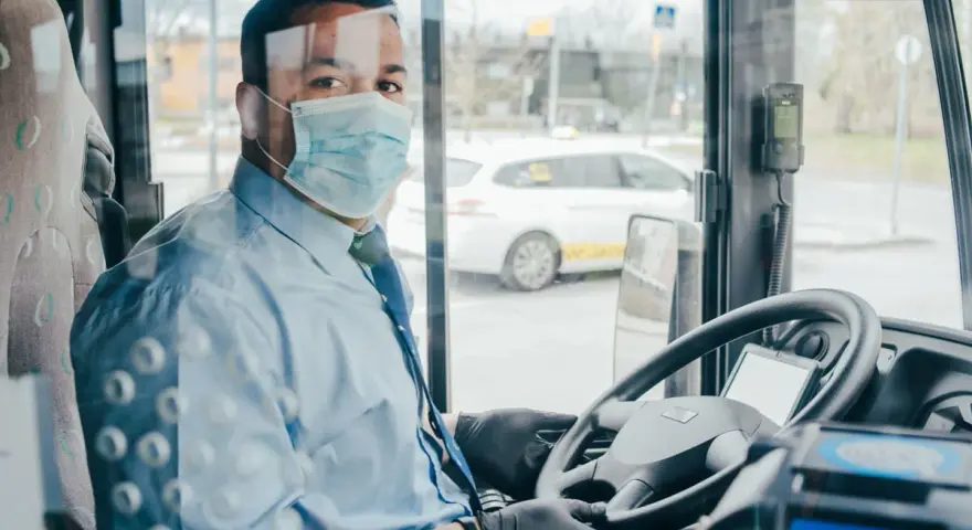 Kierowca autokaru w masce i rękawiczkach za kierownicą. Zapytaj o wynajem autokaru cena.