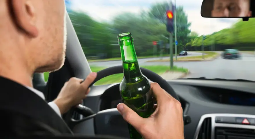 Kierowca z butelką piwa w ręku, jadący na czerwonym świetle. Grozi mu konfiskata samochodu.