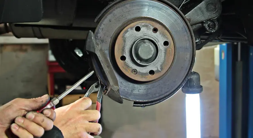 Dłonie mechanika z narzędziami przy hamulcu tarczowym samochodu.