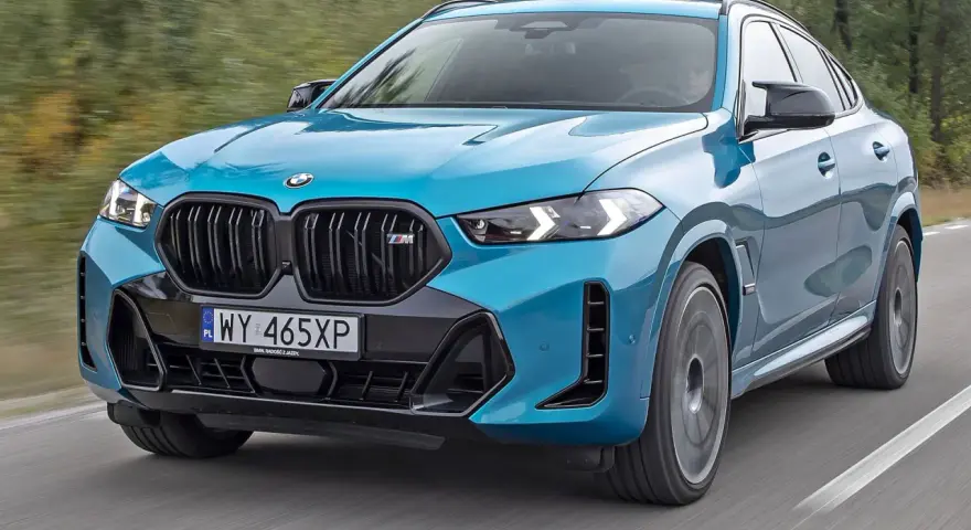 Niebieskie x6 BMW M na drodze, z rozmytym tłem lasu.