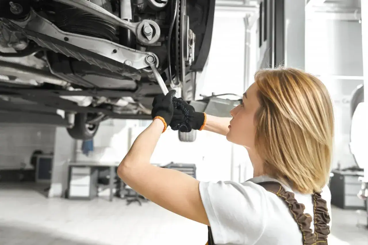 Mechaniczka pracuje pod samochodem, dokręcając śrubę wahacza. Sprawdza wymiana wahacza cena.