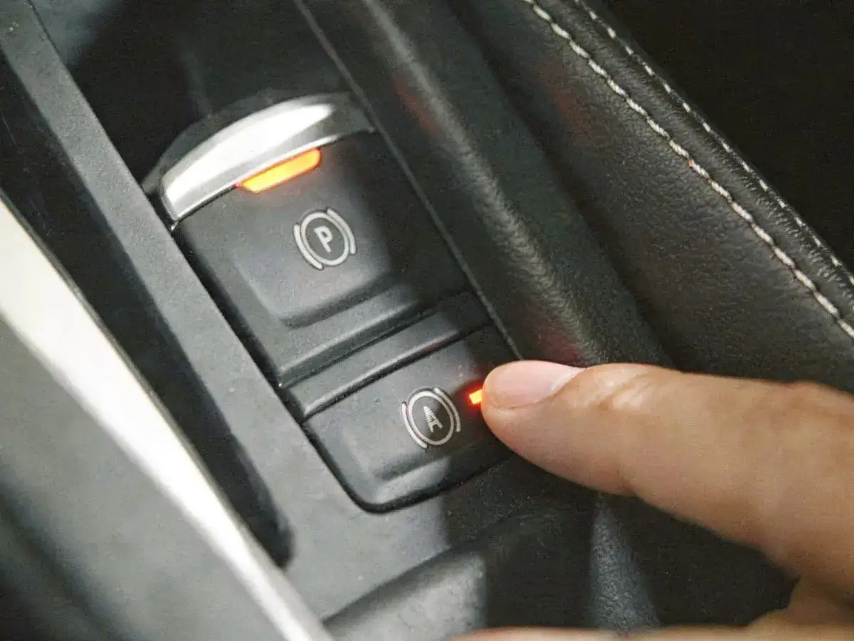 Dłoń naciska przycisk z ikoną hamulca ręcznego, aktywując funkcję auto hold.