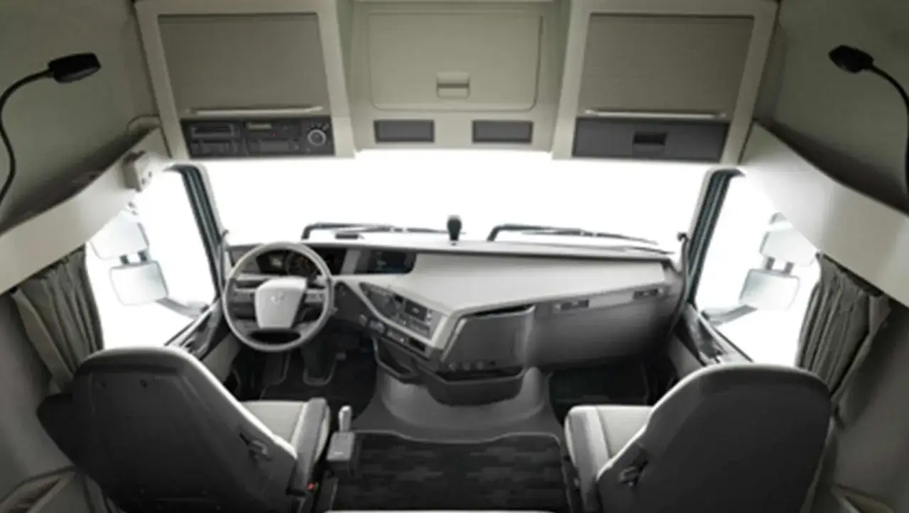 Wnętrze kabiny Volvo FH12 z dwoma fotelami, deską rozdzielczą i kierownicą.