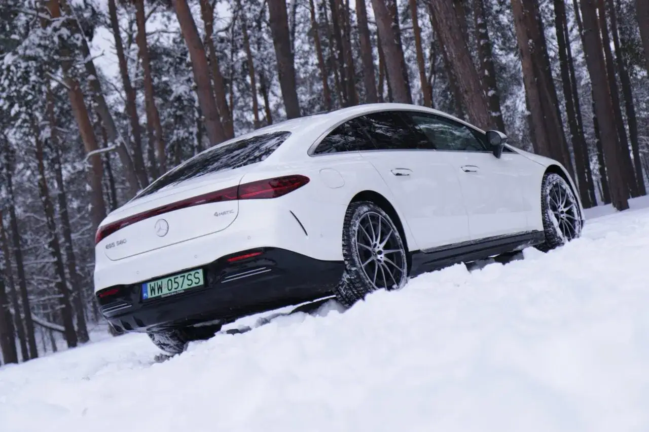Biały Mercedes EQS 580 4Matic wjeżdża w zaspy śnieżne w zimowym lesie.