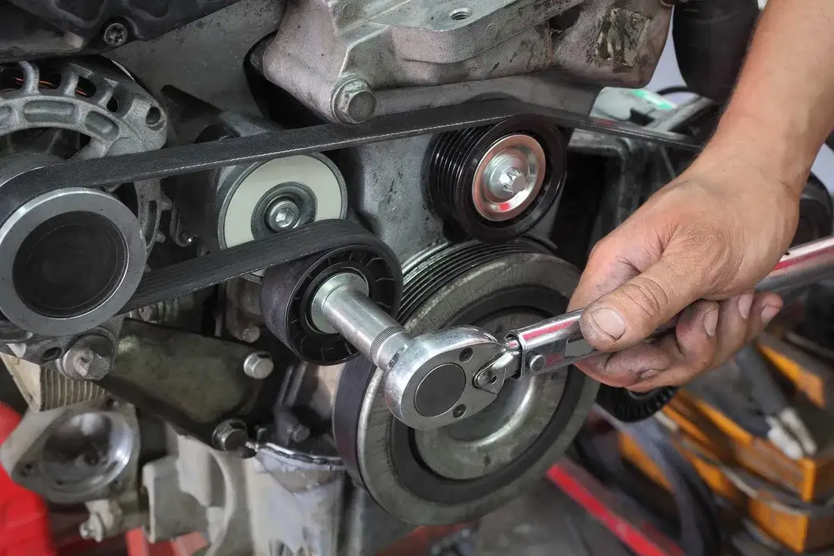 Mechanik dokonuje wymiany paska klinowego, używając klucza dynamometrycznego do napinacza.