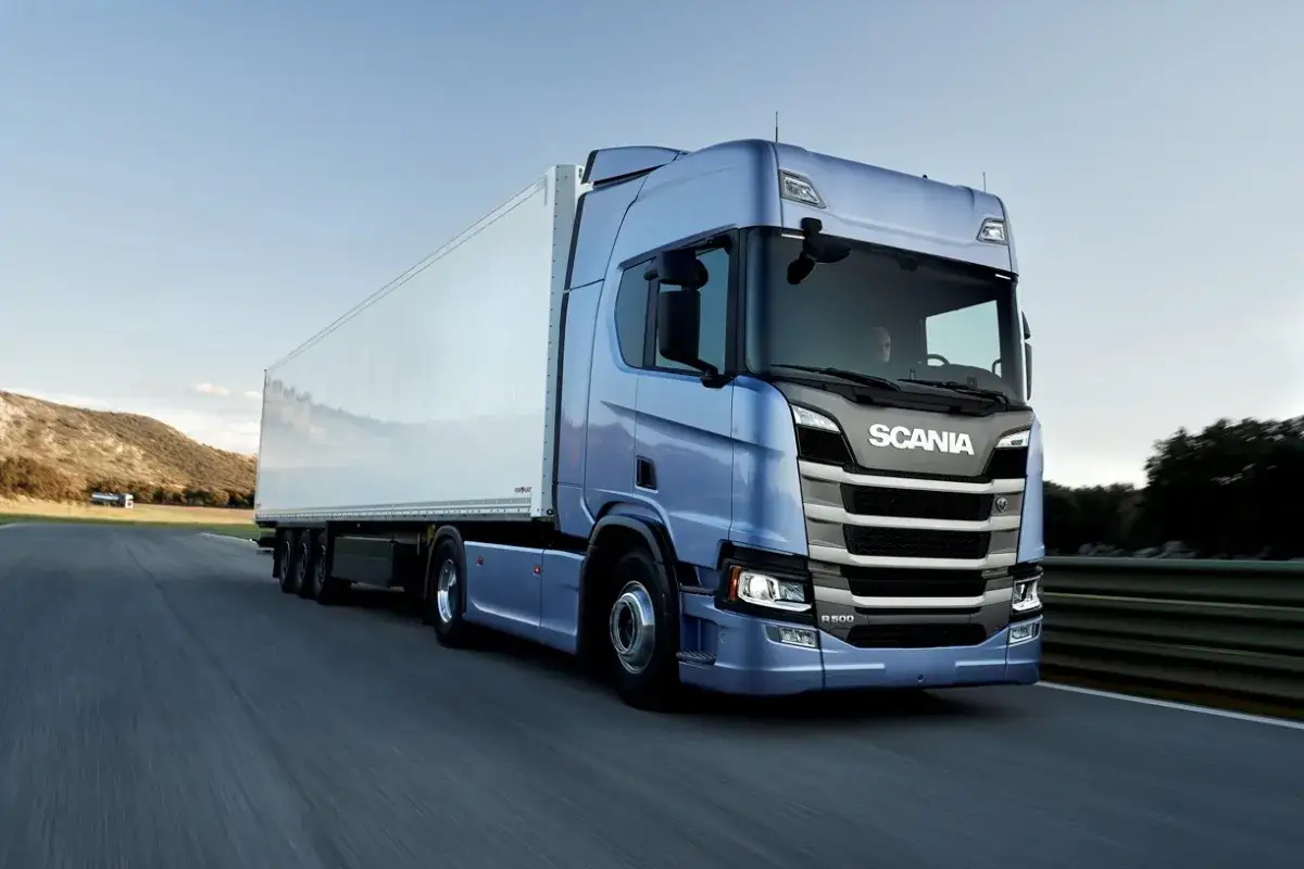 Niebieska Scania T z białą naczepą jedzie po pustej drodze.