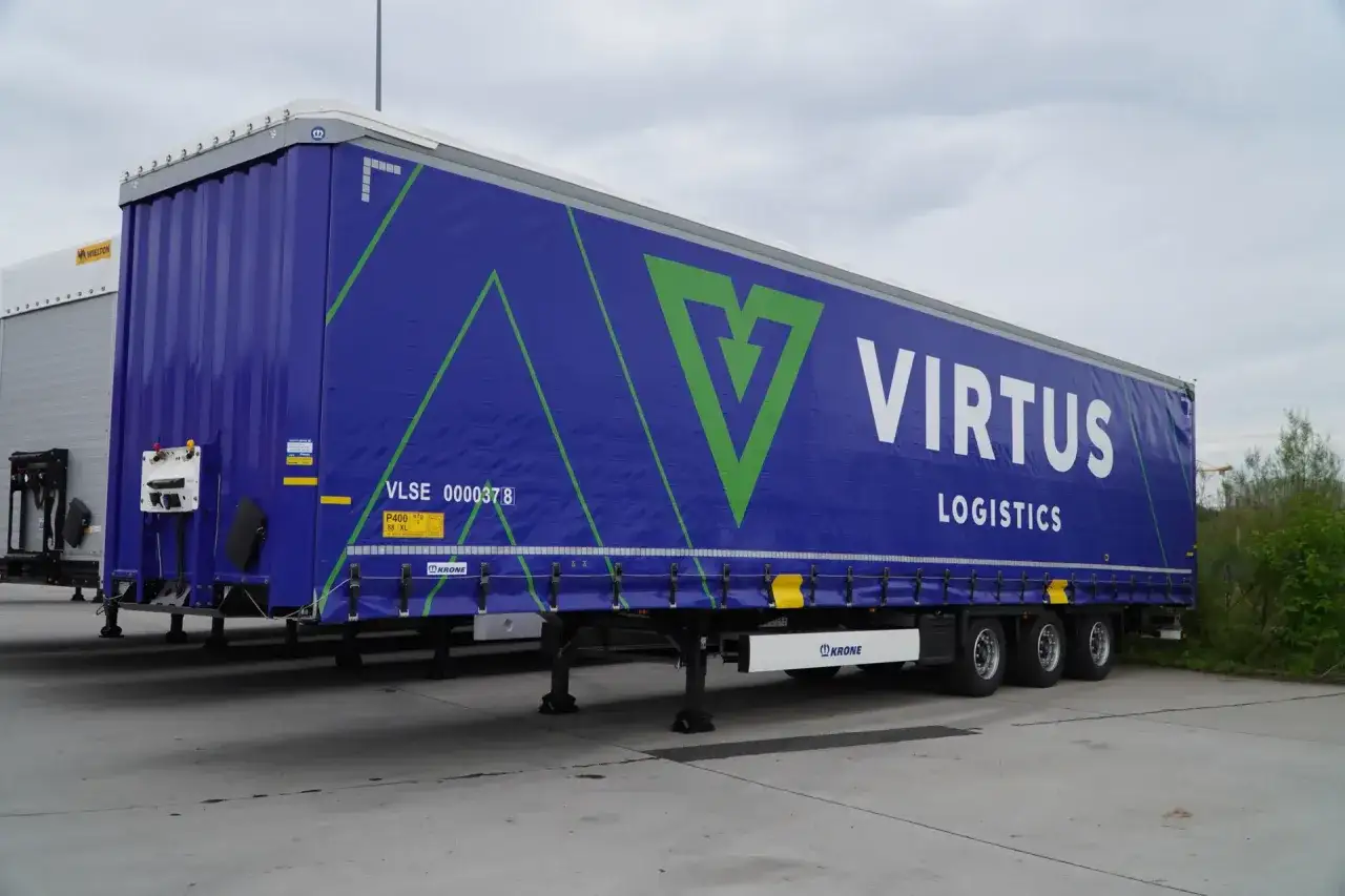 Niebieska naczepa z logo VIRTUS LOGISTICS. W tle widać inną naczepę i drzewa.
