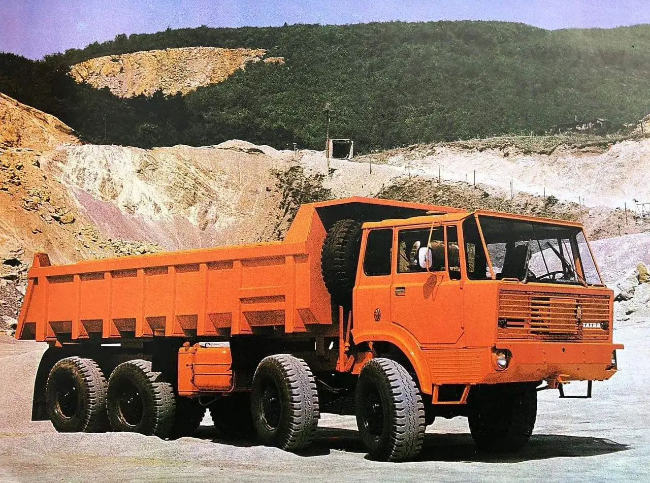 Pomarańczowa wywrotka Tatra 813 z zapasowym kołem na pace, gotowa do pracy w kamieniołomie.