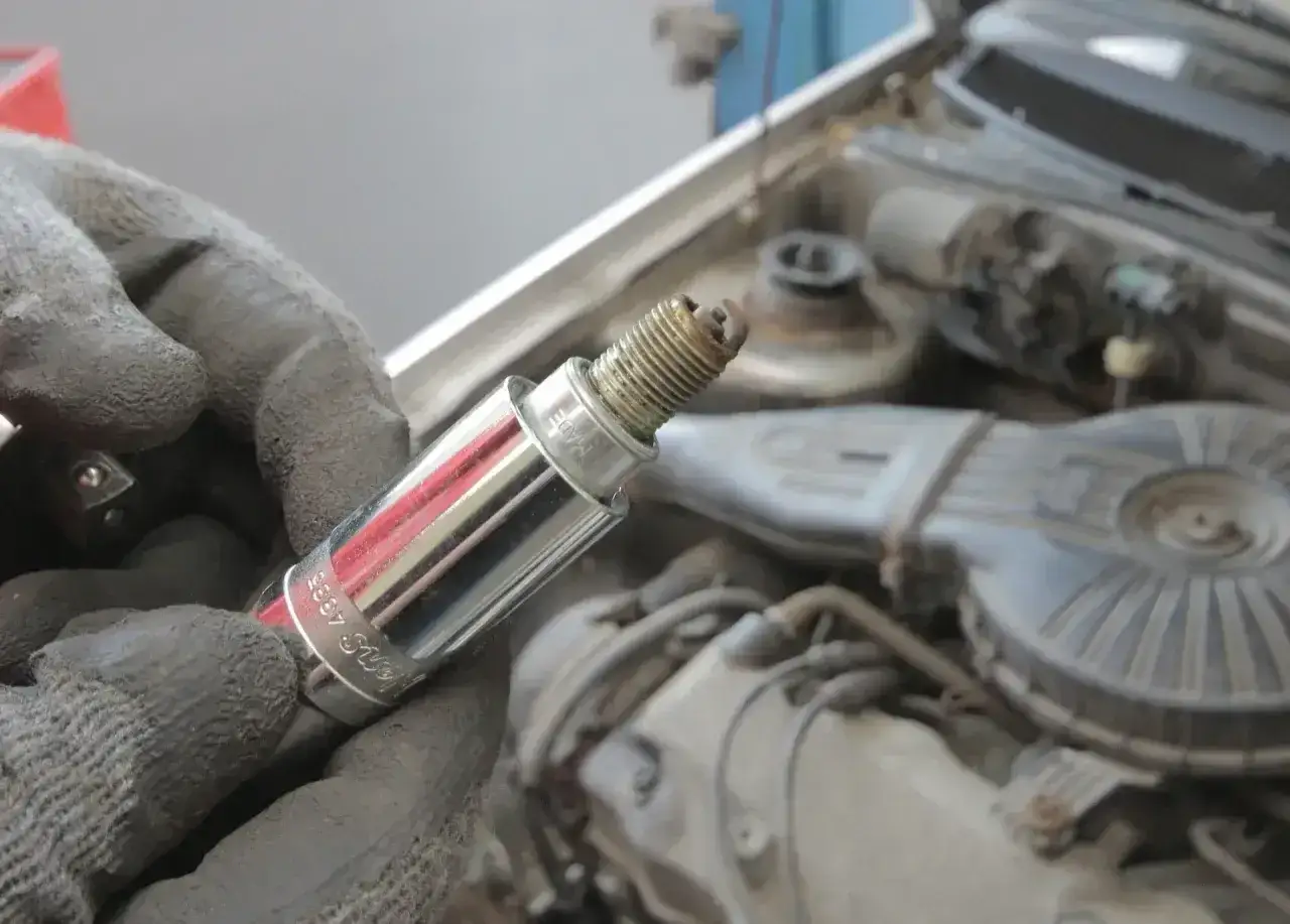 Rękawica trzyma świecę zapłonową, potencjalnie przyczynę błędu dtc p0300 renault. Silnik w tle.